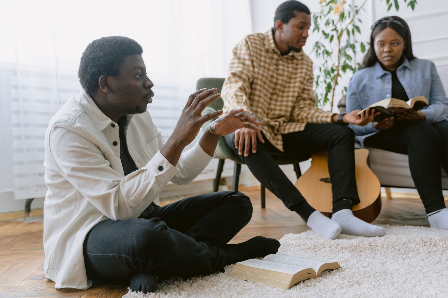 Three people talking over open Bibles in a living room