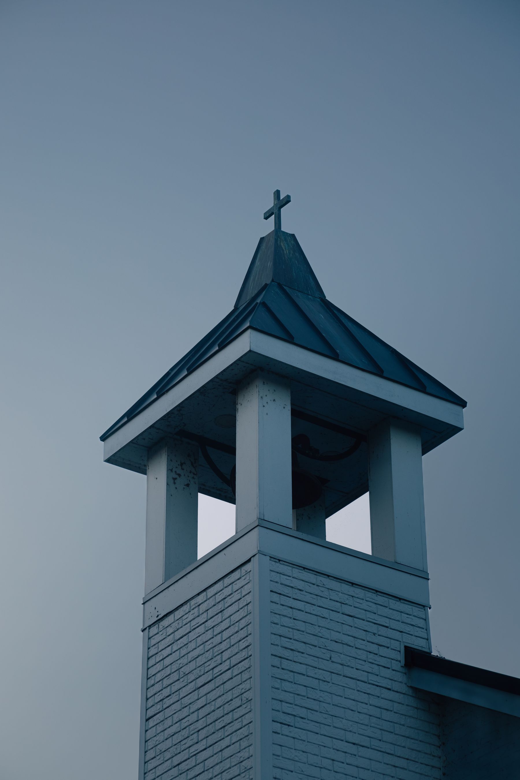 A white bell tower with a cross against a blue evening sky