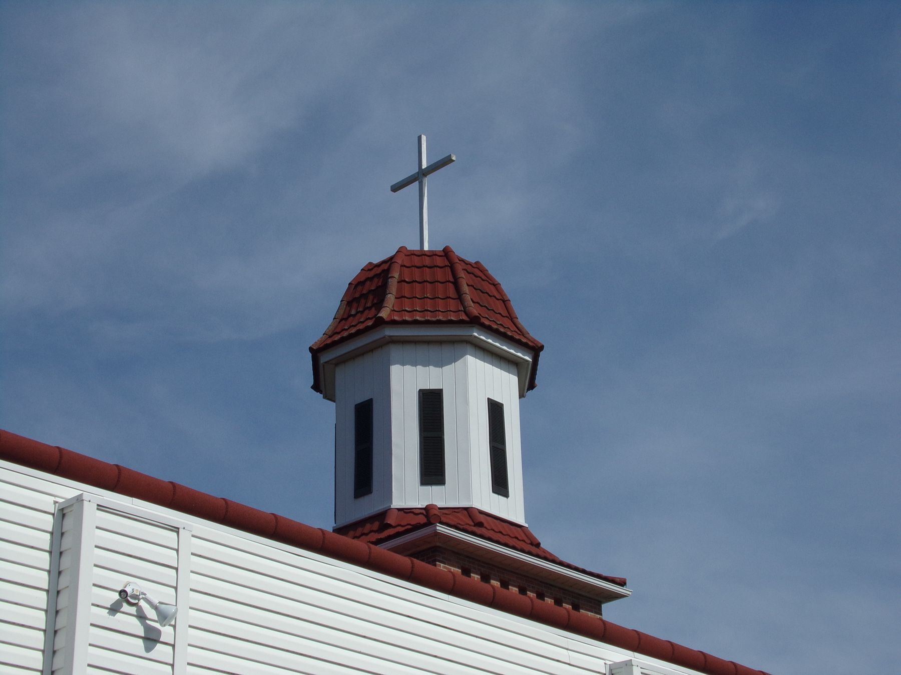 A white church steeple with a cross against a blue sky