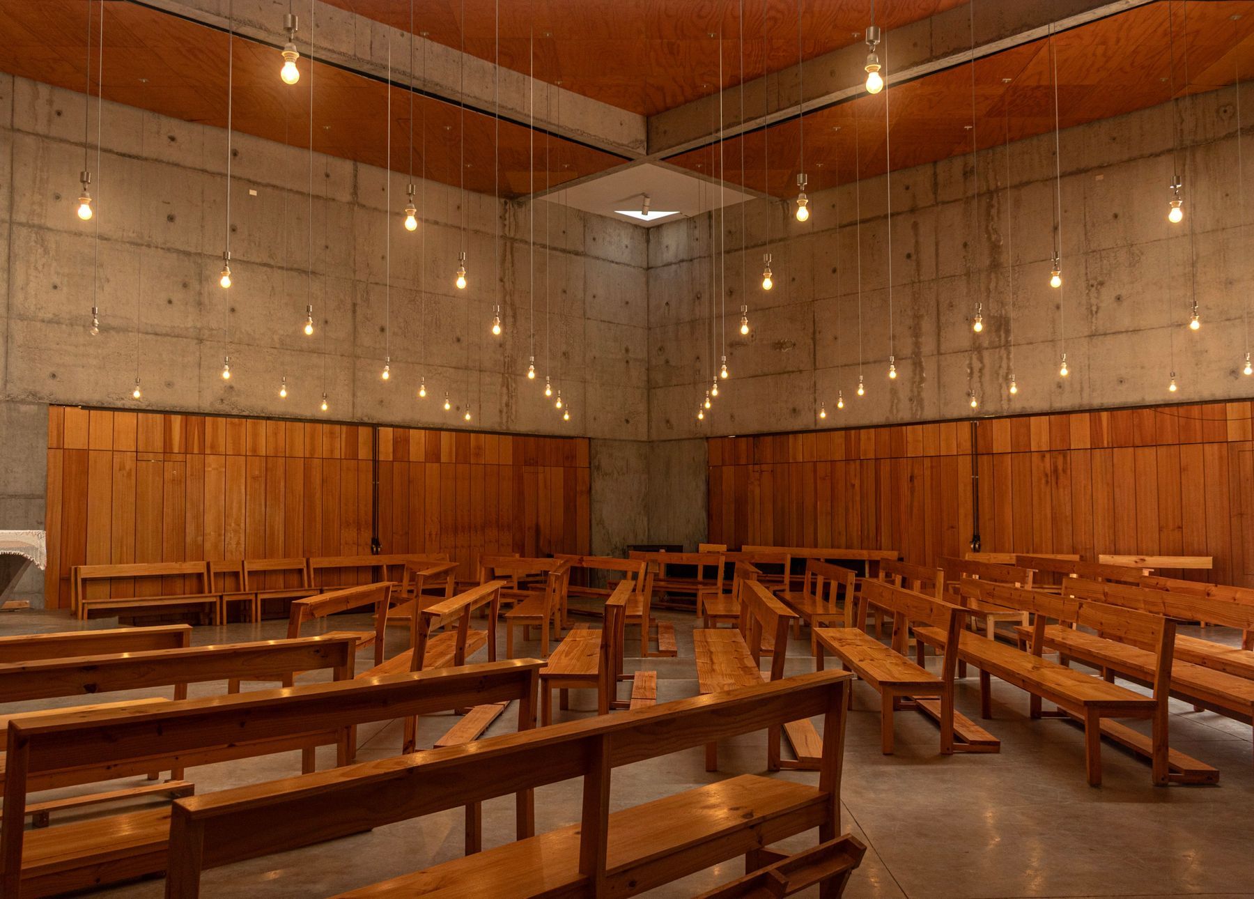A warm wooden worship hall with rows of benches under hanging lights